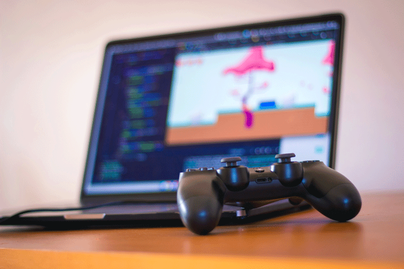 A laptop monitor with a game on the screen and a video game controller